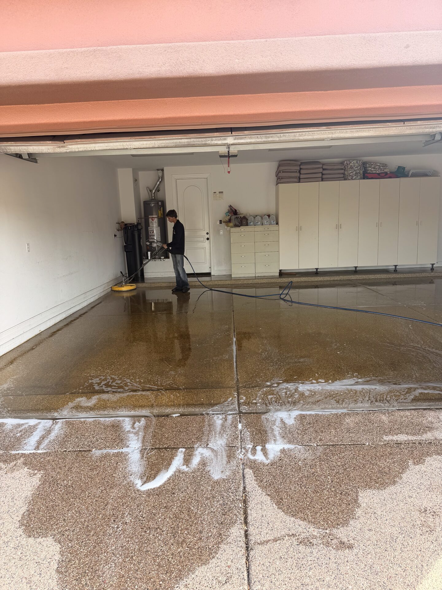 A garage floor mid-clean, suds marking the line between washed concrete and the section still to be done
