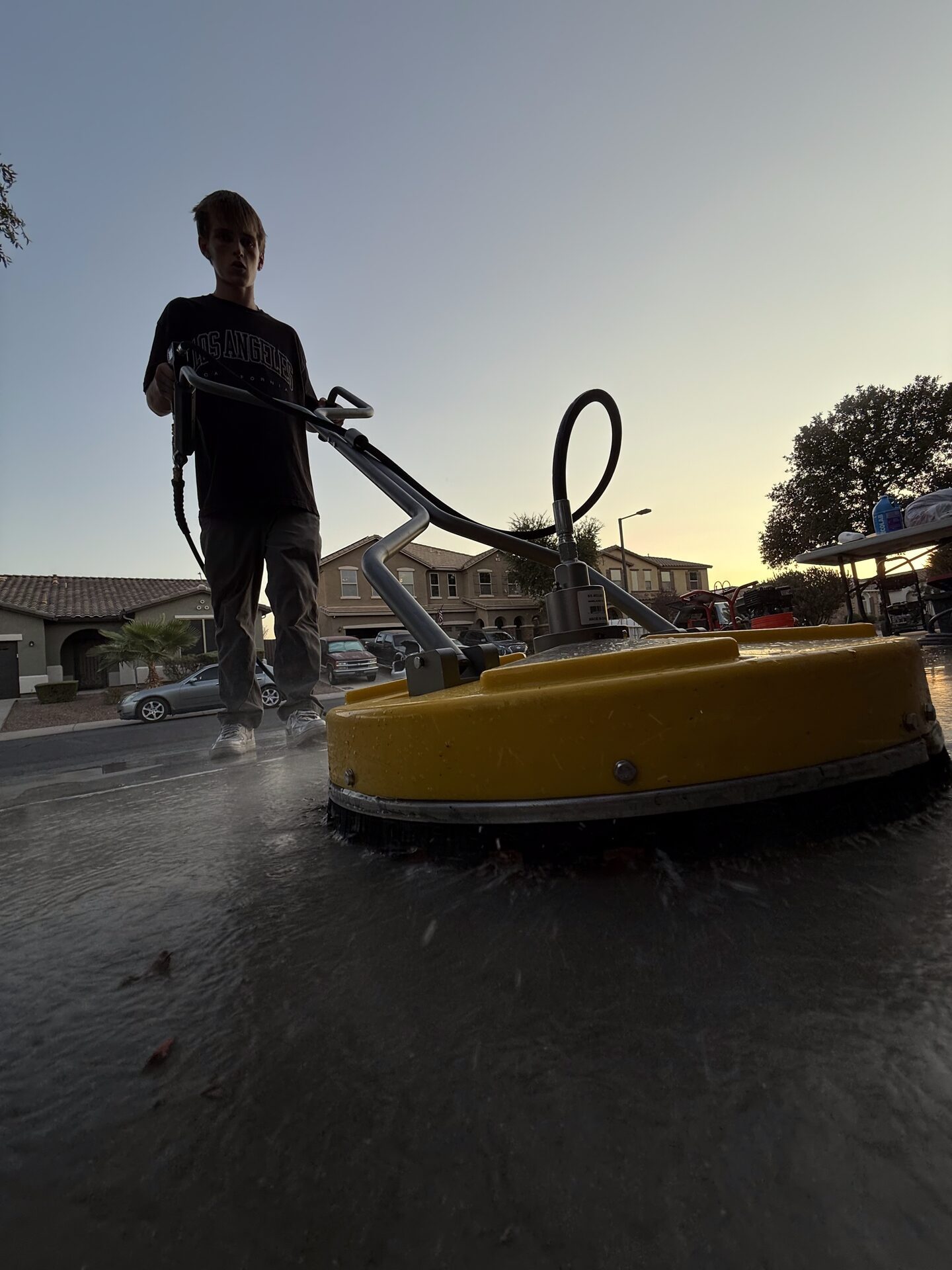 A surface cleaner at work on a driveway at dusk, backlit by the setting sun