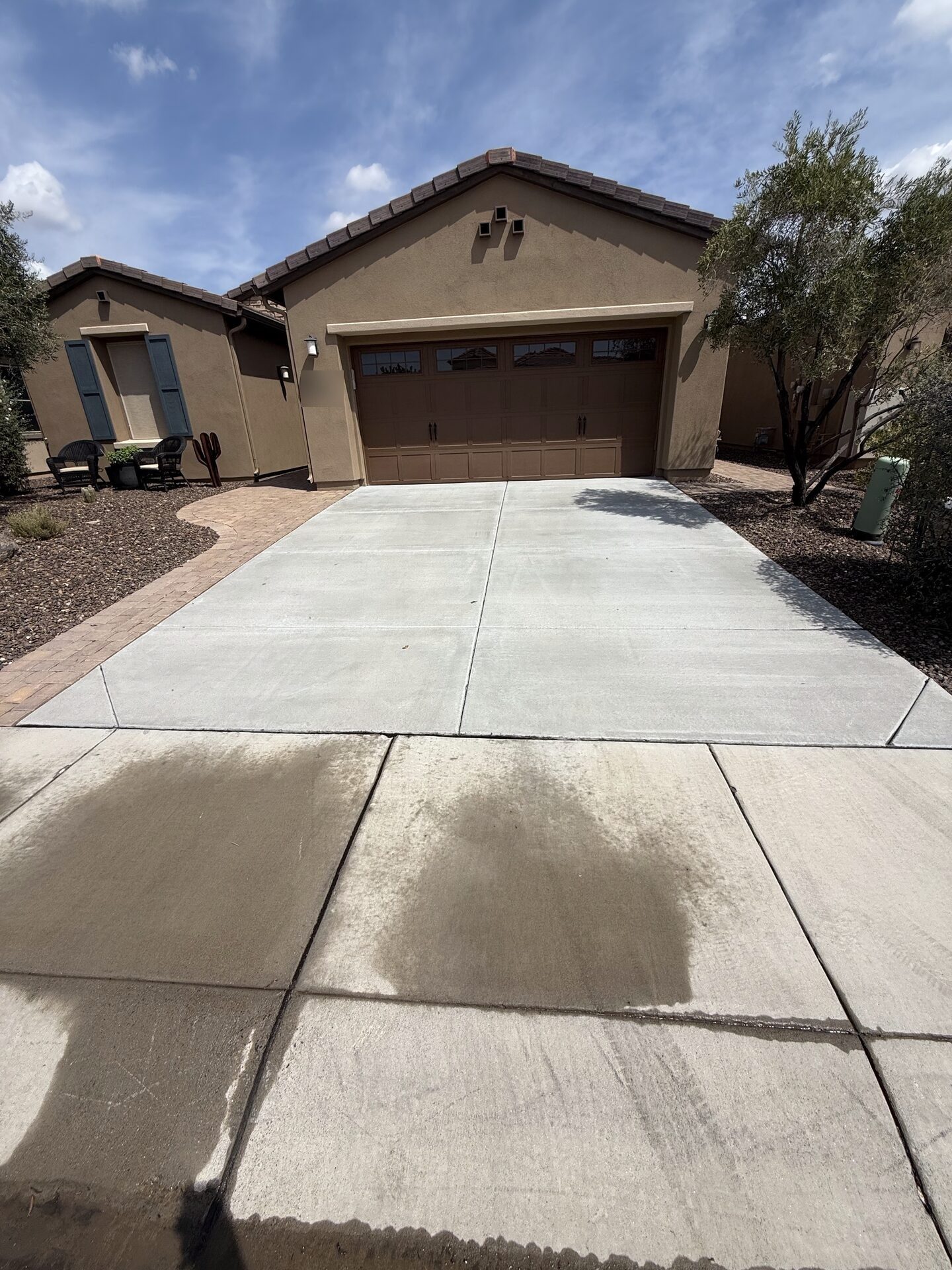 A driveway partway through a pressure wash: the upper half cleaned back to pale concrete, the lower half still darkened with built-up grime