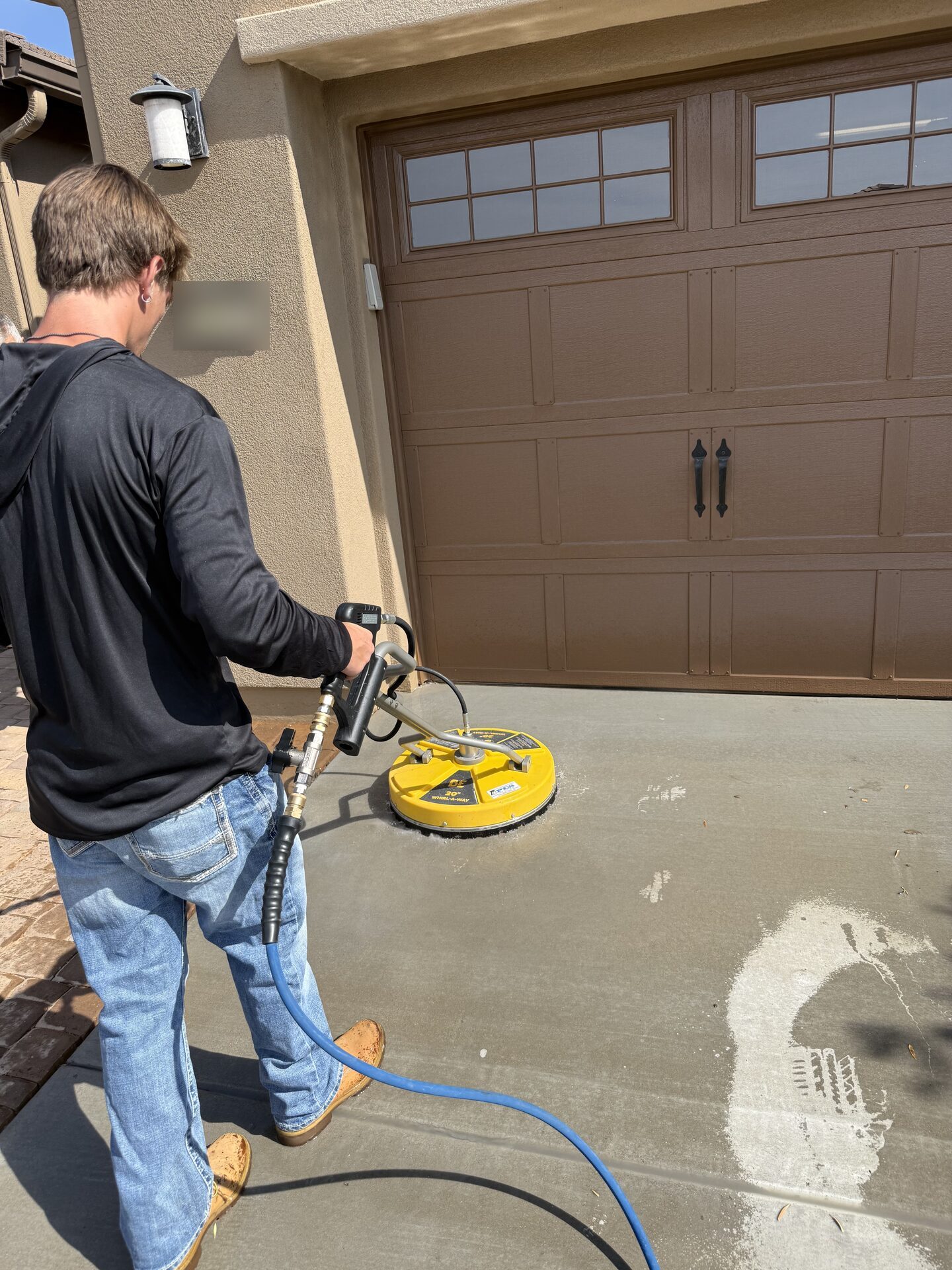 Close view of a REBEL crew member steering the surface cleaner along a driveway beside the garage